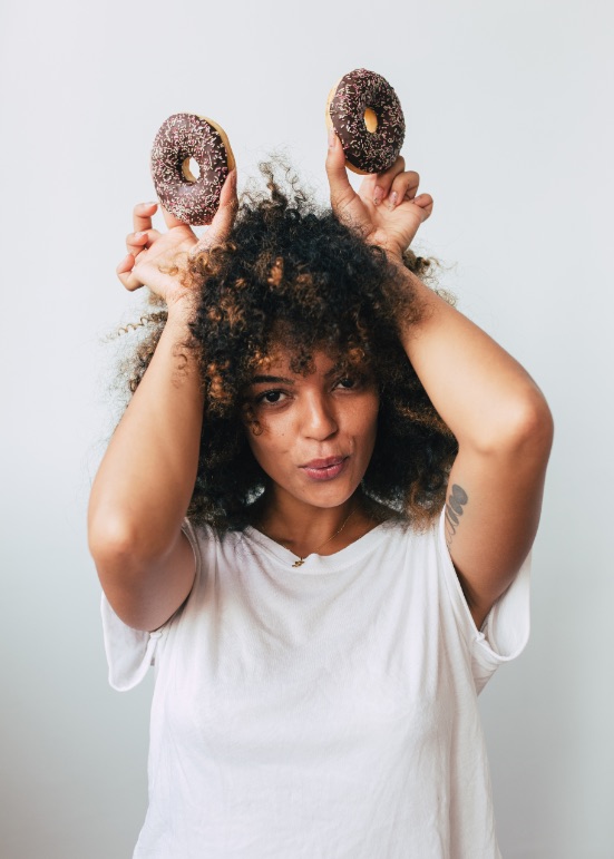 Young woman goofing around, holding two chocolate doughnuts over her head like bunny ears.